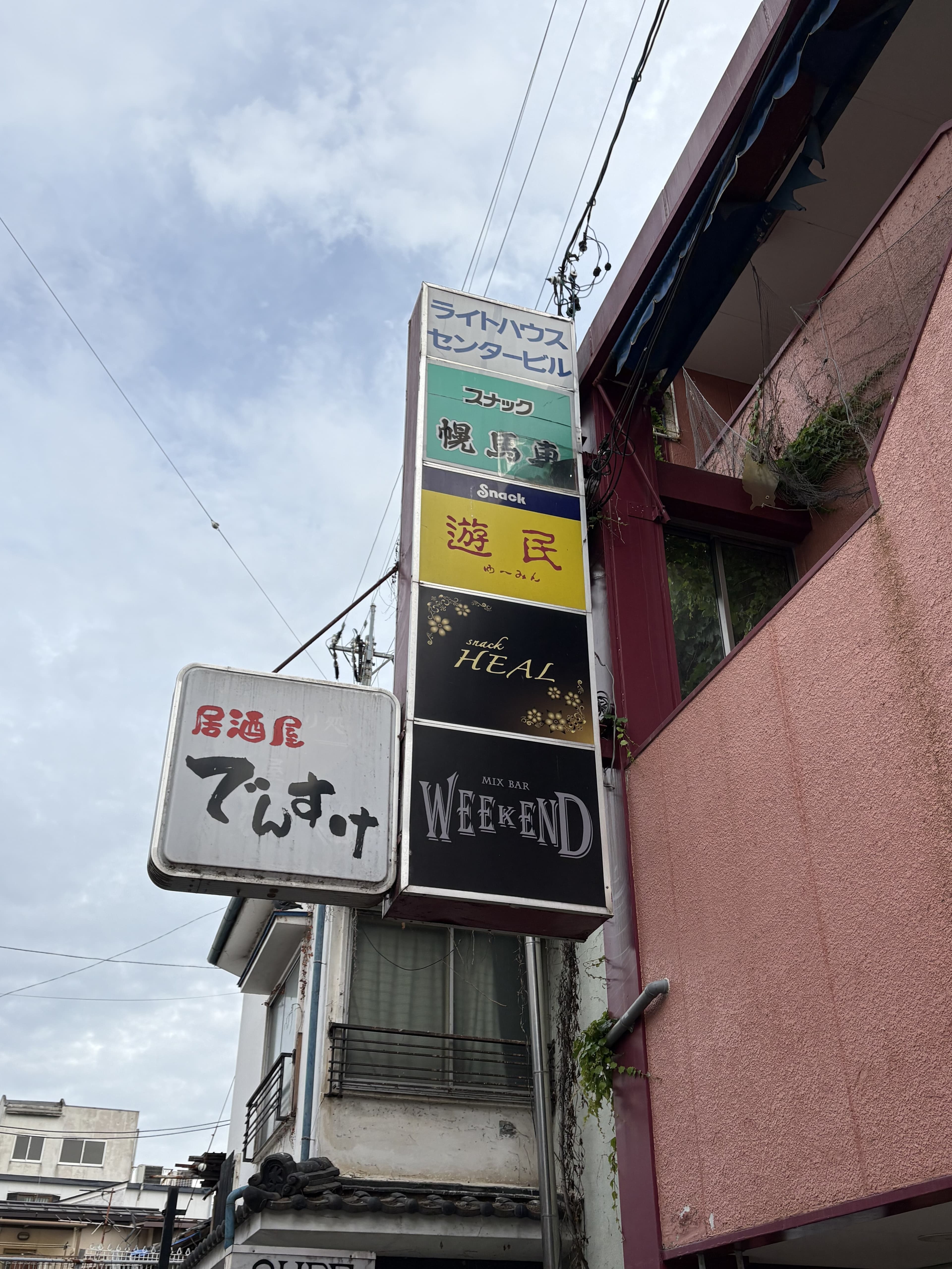 上田市中心部の外壁に突き出す「でぃす」「HEAL」「WEEKEND」などの縦並び看板