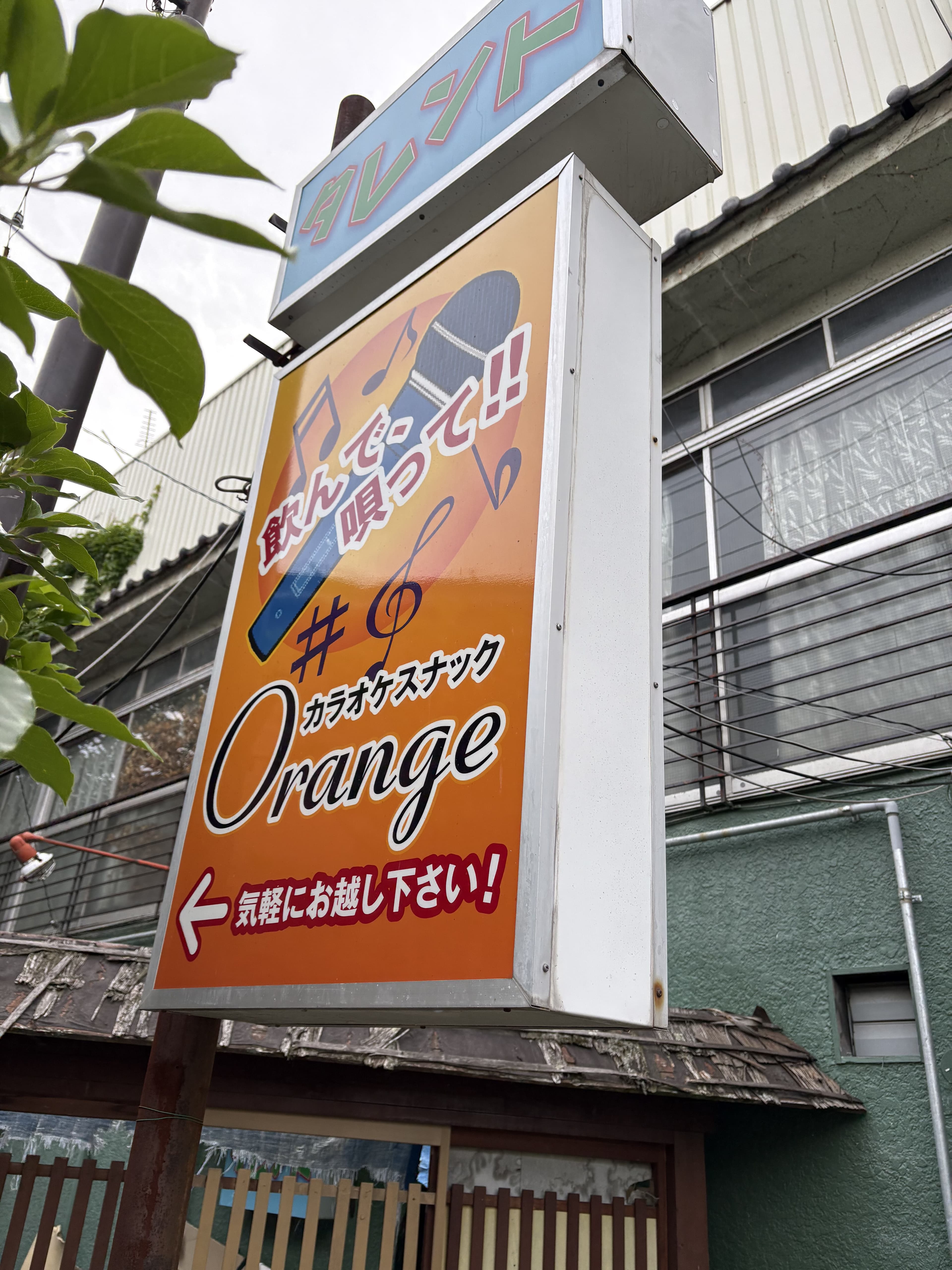 オレンジ色の縦看板に音符を散らした「カラオケスナック Orange」