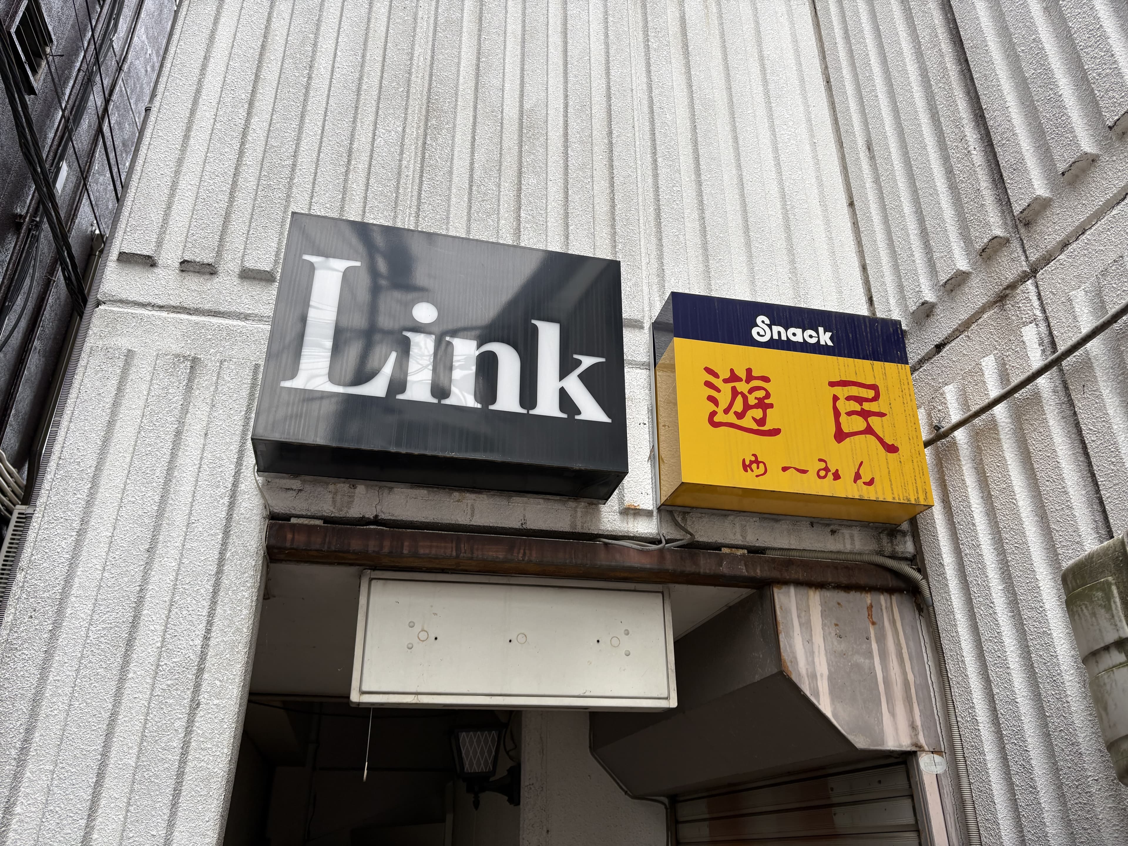 入口上に並ぶ黒い「Link」と黄色い「Snack 遊民」の看板