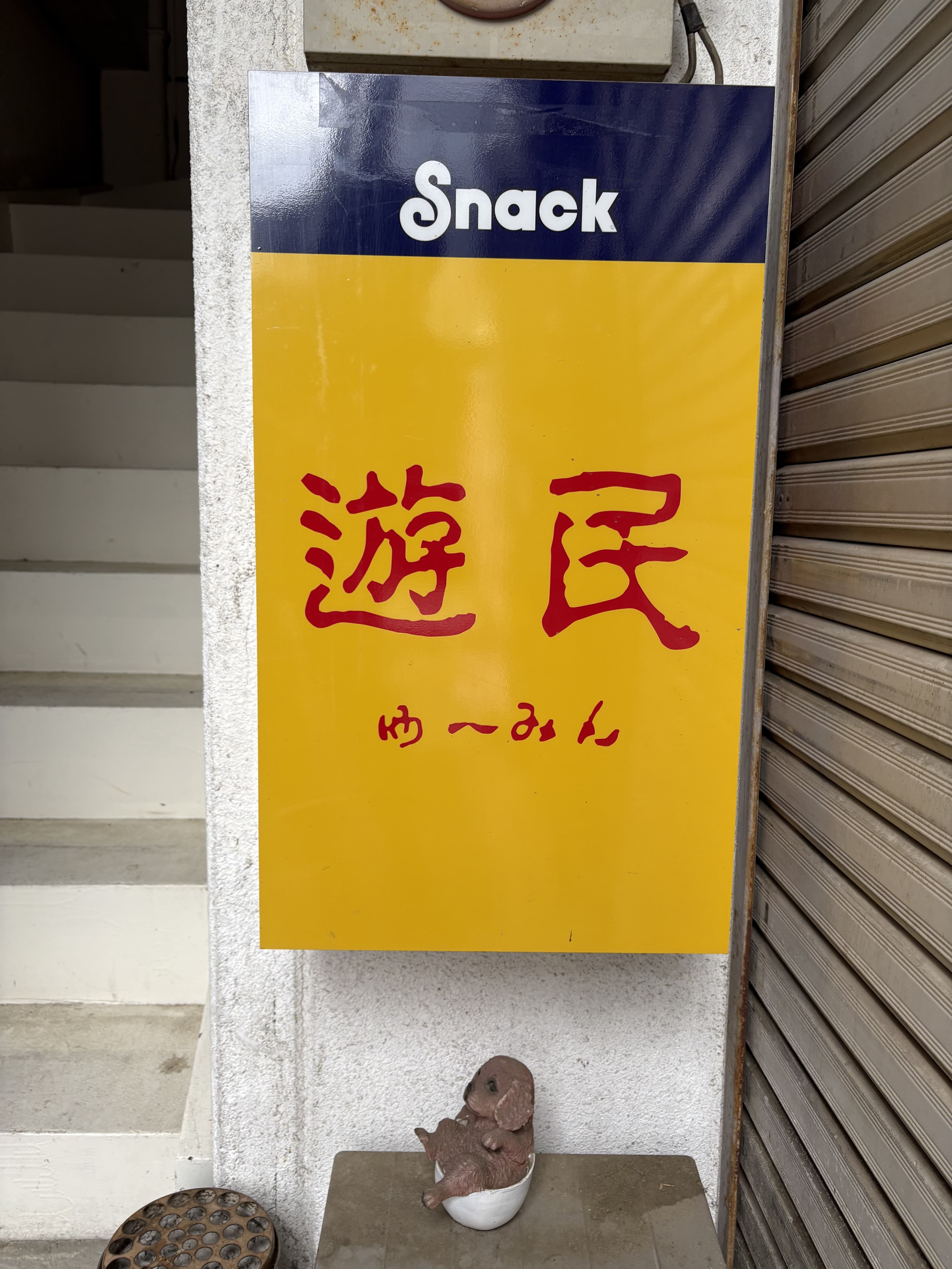 階段脇に掛けられた黄色い「Snack 遊民」看板