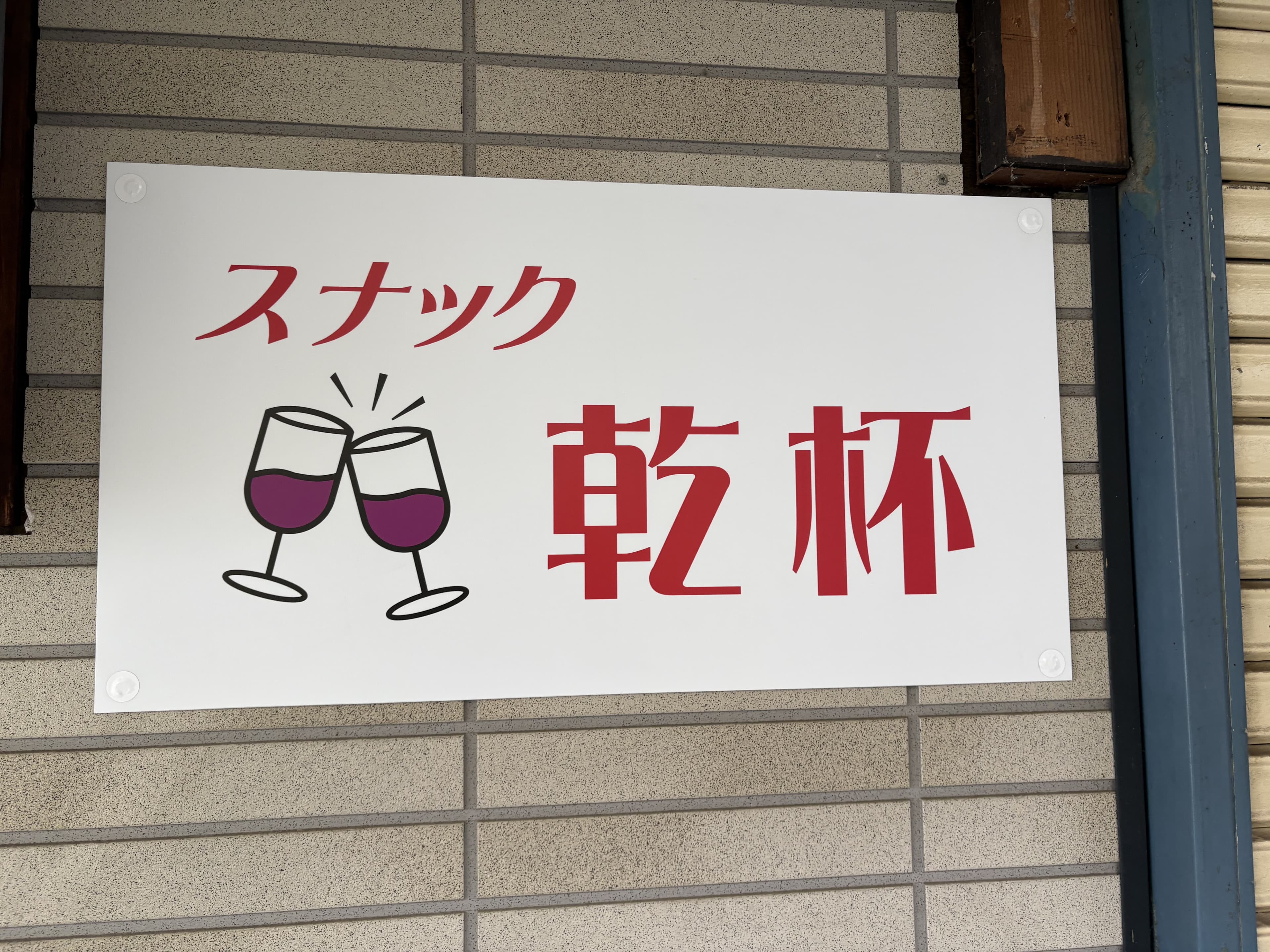 グラスのイラストを添えた白い「スナック 乾杯」看板