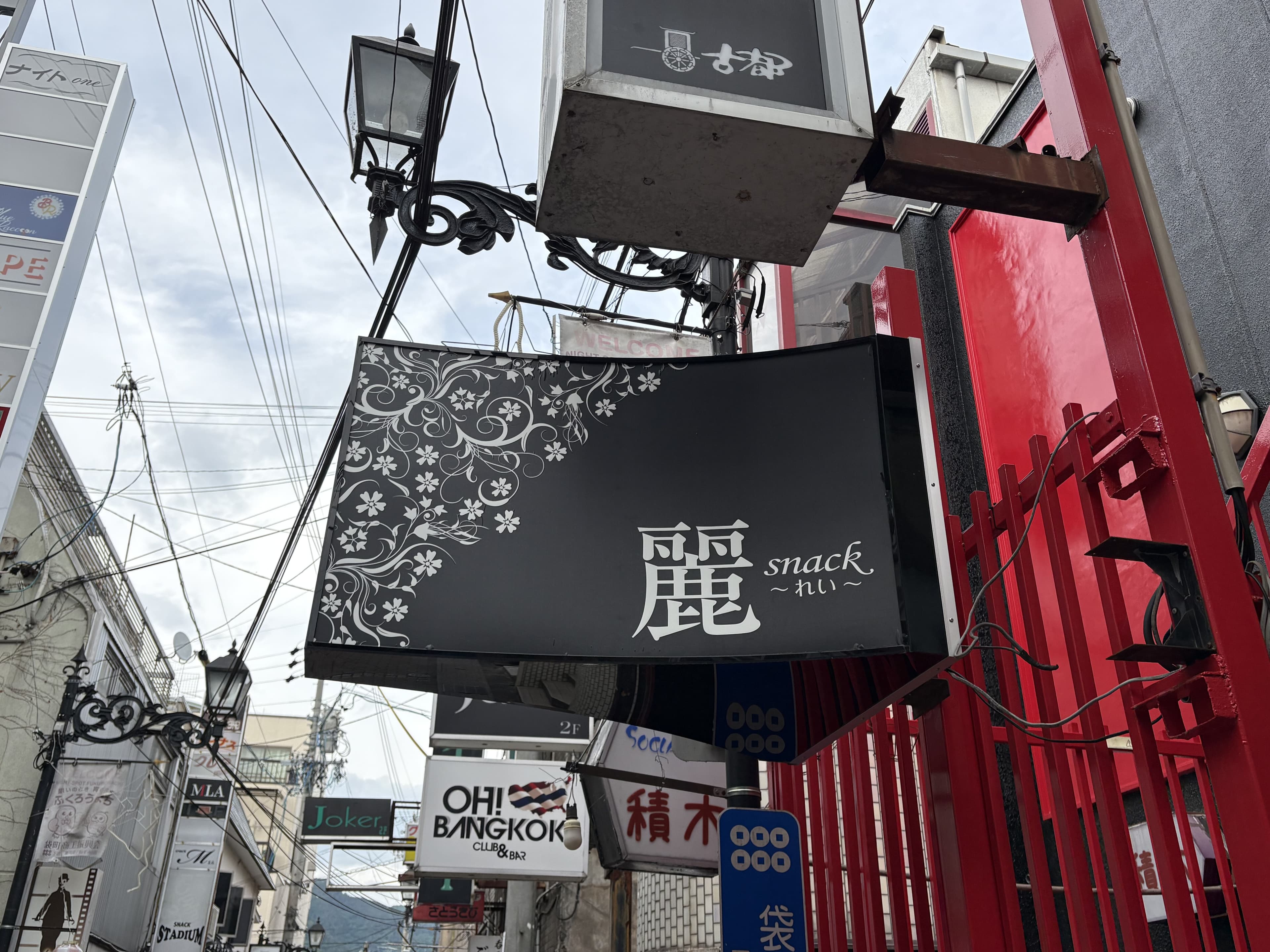黒い袖看板に白い花模様を添えた「麗 snack」看板
