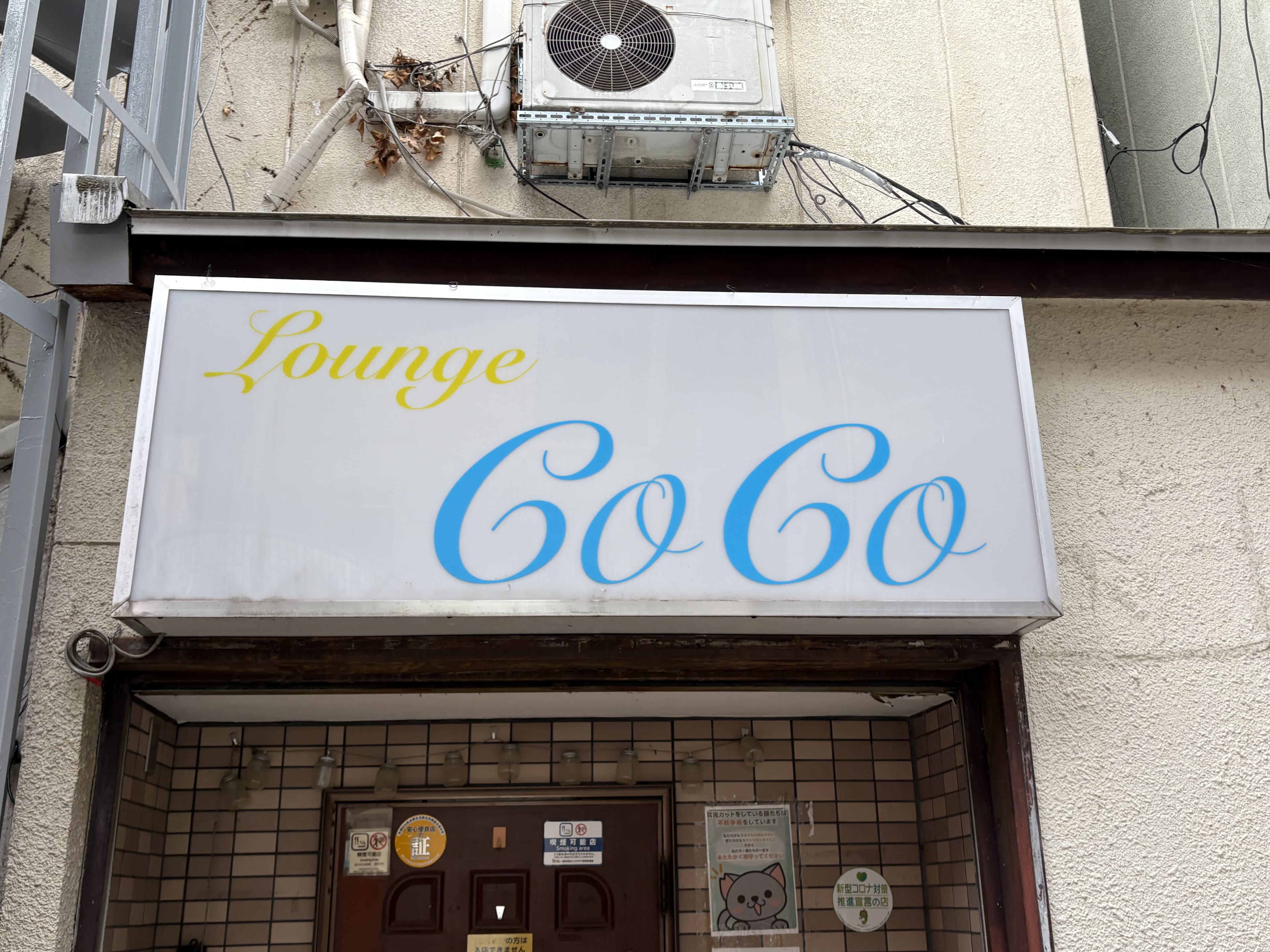 白地に水色の筆記体を置いた「Lounge CoCo」看板