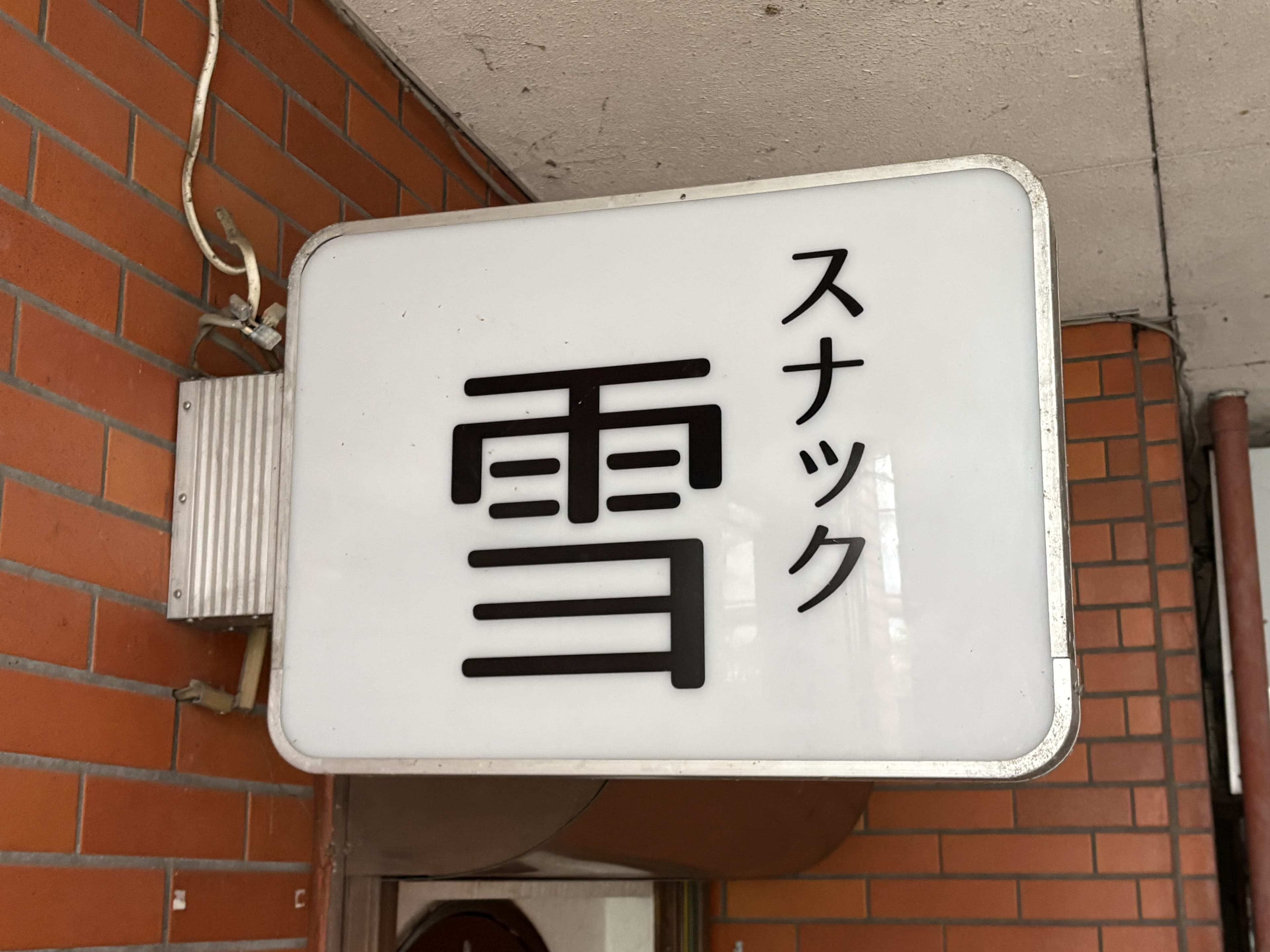 白い箱看板に太い黒文字を置いた「スナック 雪」