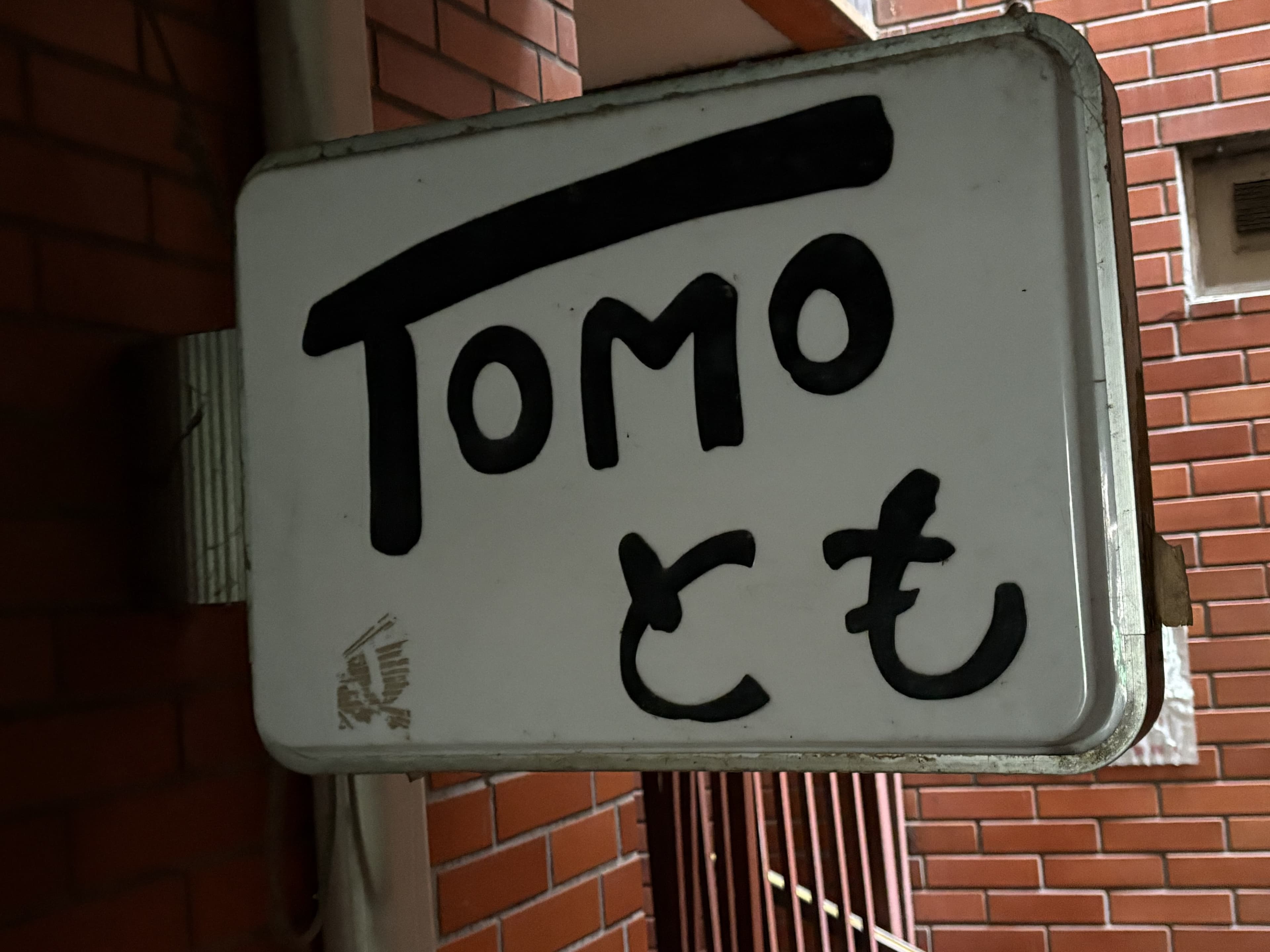 手書き風の黒文字が目立つ白い「TOMO とも」看板