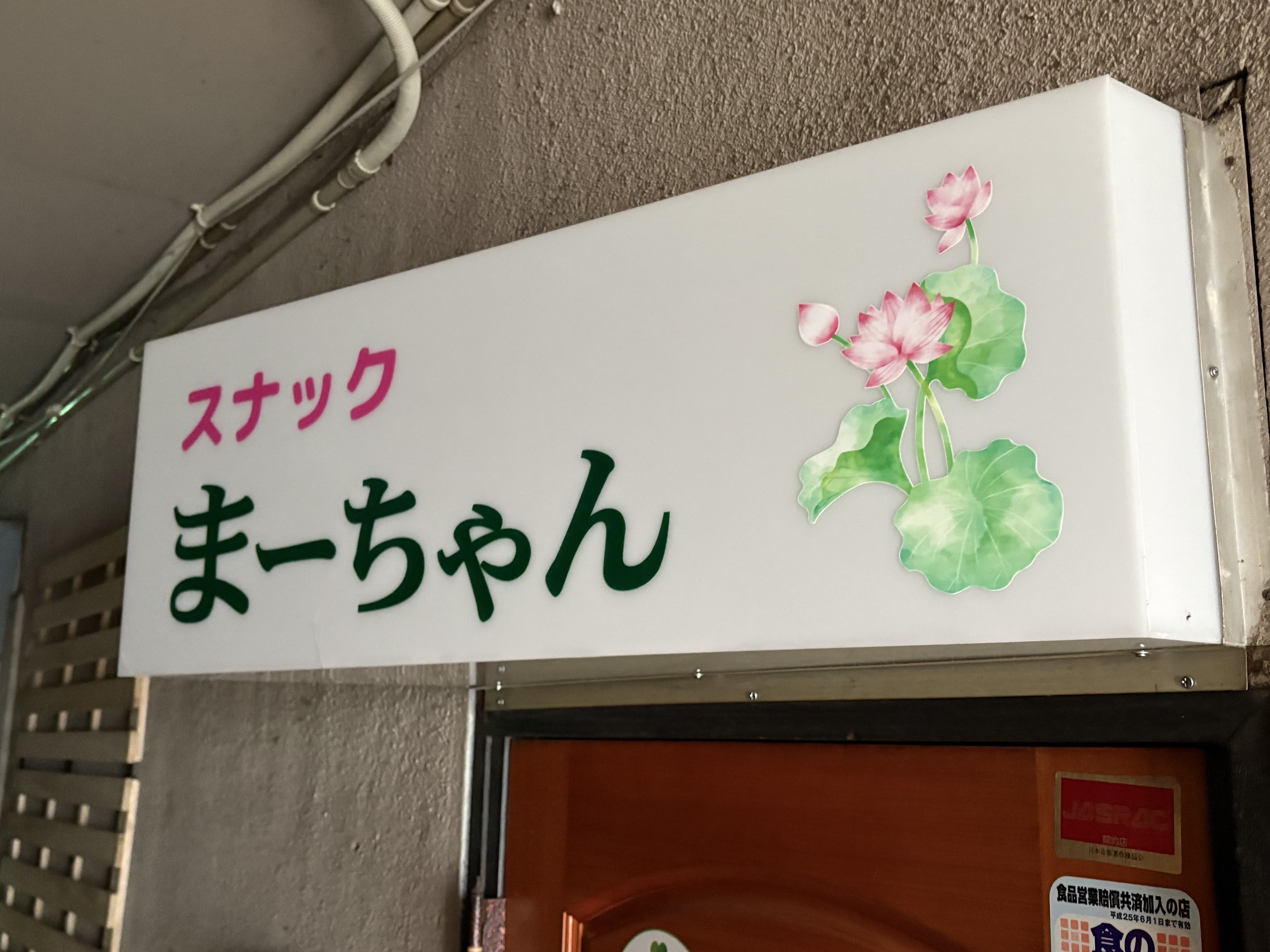 花のイラストを添えた白い「スナック まーちゃん」入口看板