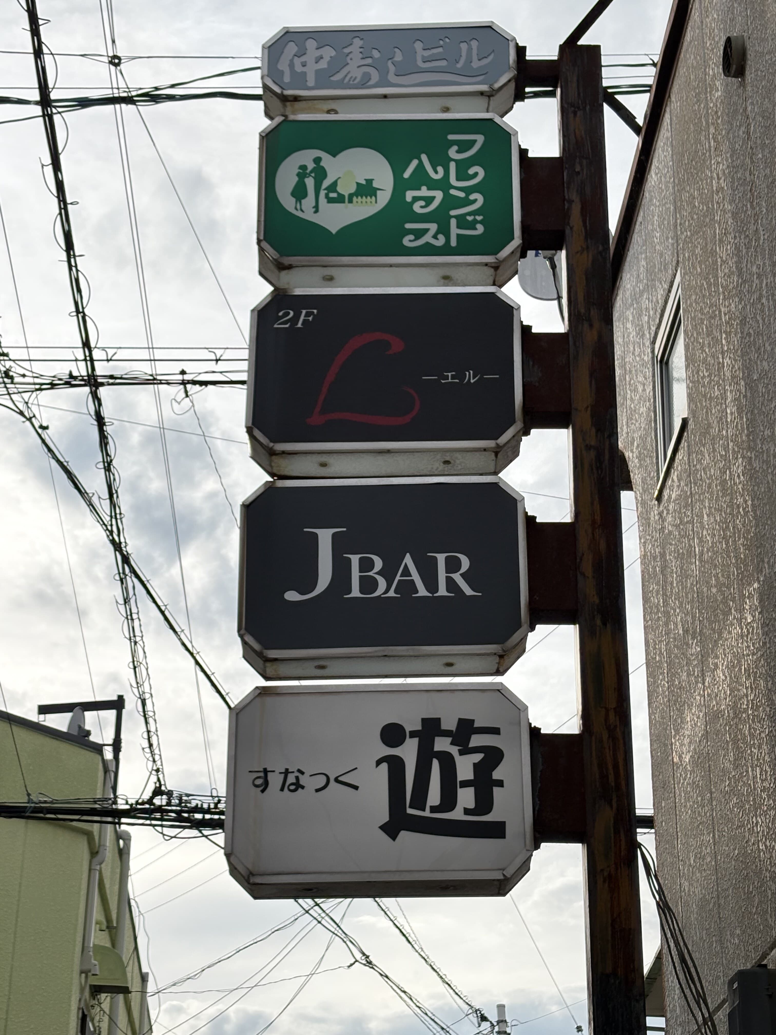 「フレンドハウス」「J BAR」「遊」が縦に重なる袖看板群