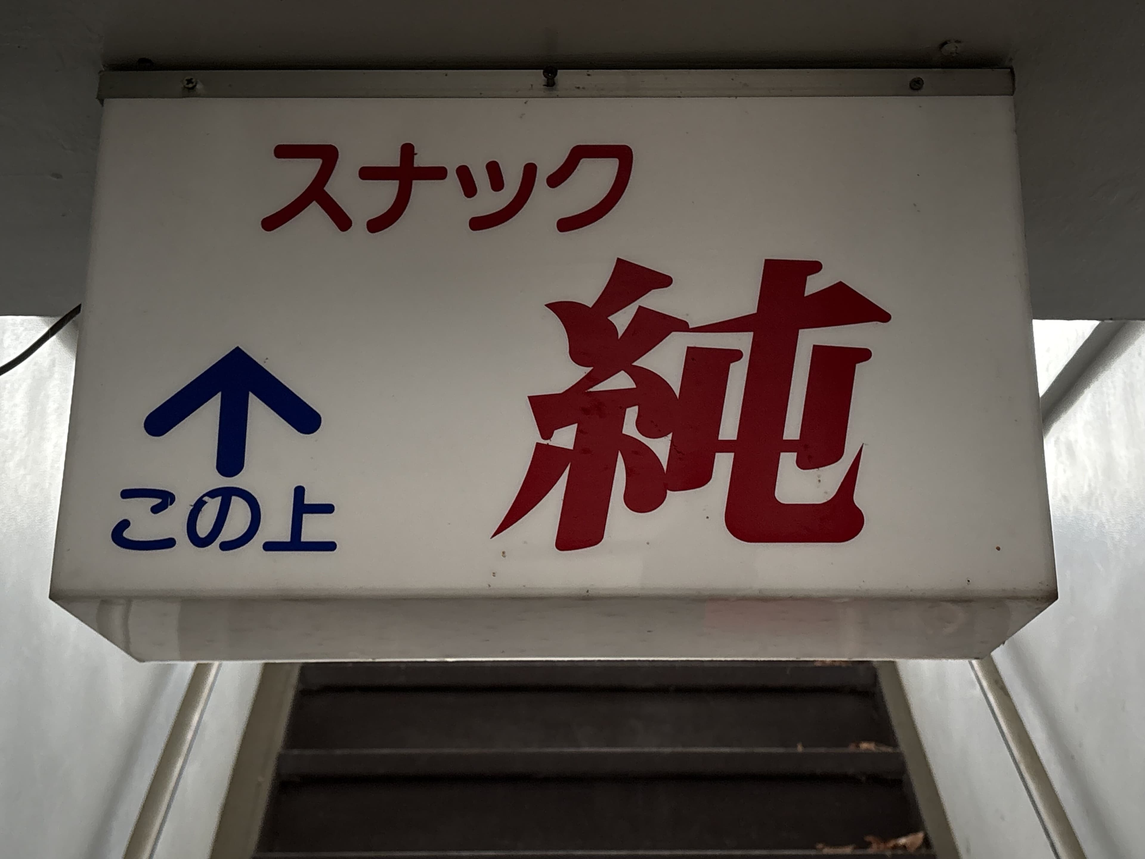 「この上」案内付きの白地「スナック 純」看板