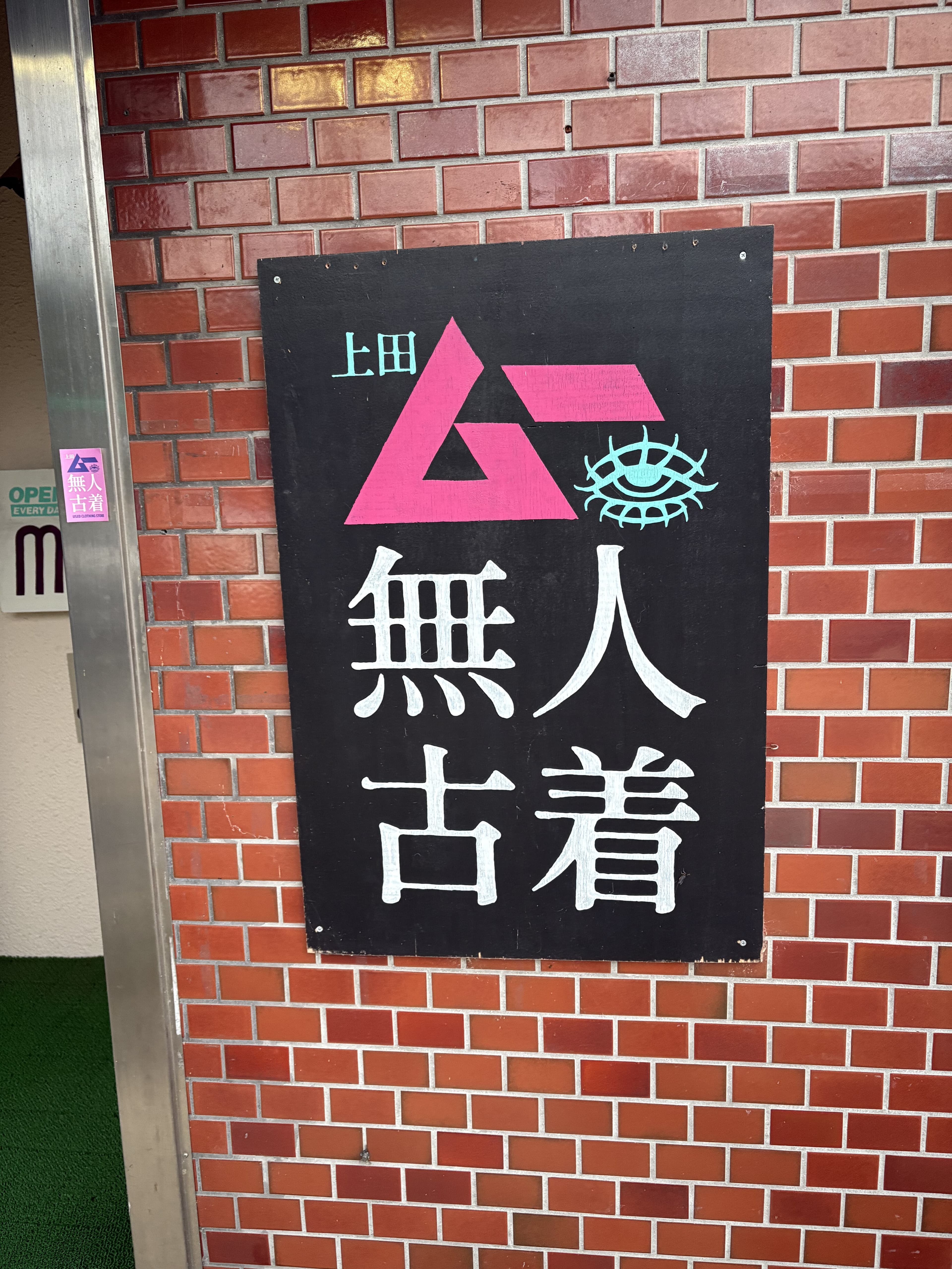 上田の煉瓦壁に掛かった『無人古着』の黒地ロゴ看板