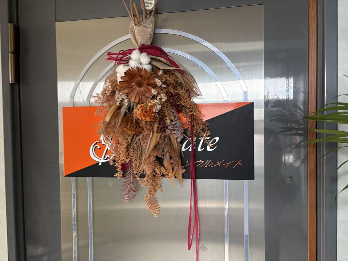 花飾りに隠れた黒とオレンジの入口看板ソウルメイト