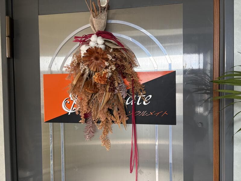 花飾りに隠れた黒とオレンジの入口看板ソウルメイト